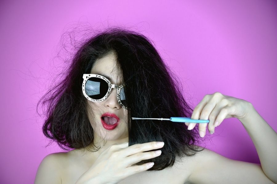 Woman cutting her hair in front of a purple background