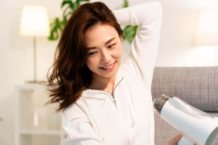 Asian woman smiling while drying her hair