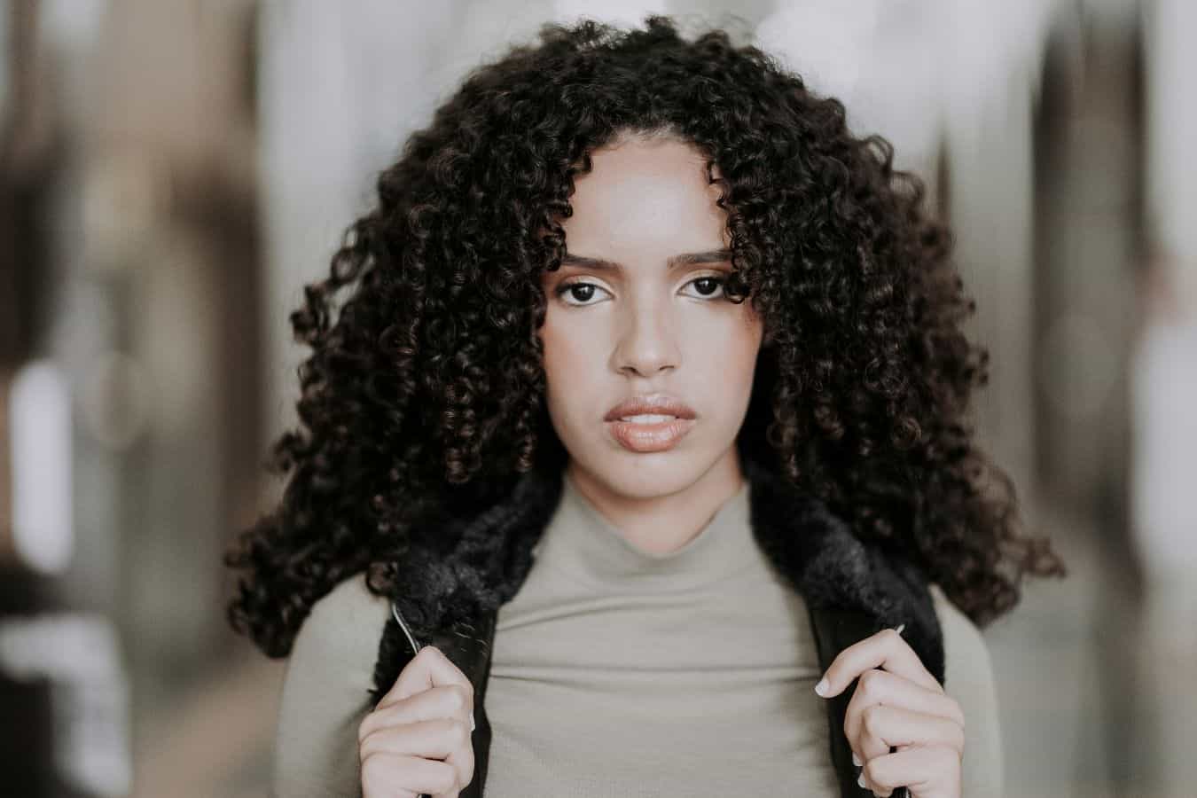 Woman with curly hair staring intently at the camera holding on to a backpack