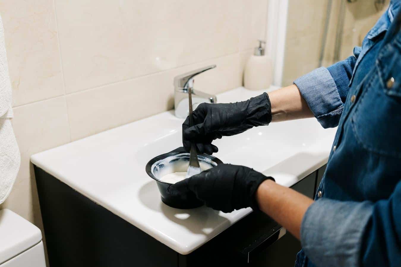 A person mixing hair dye on a sink wearing black gloves