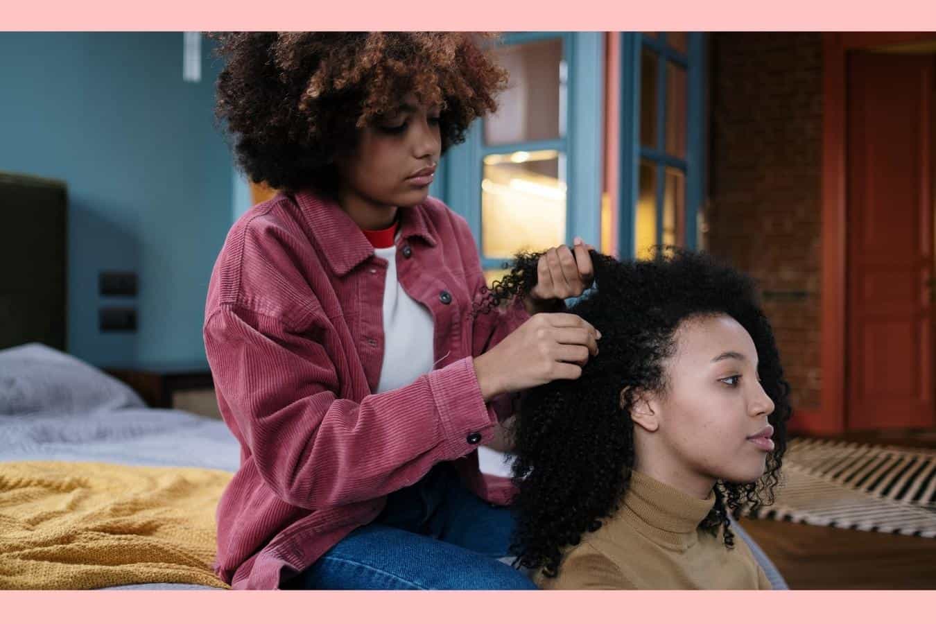 a young woman braiding another woman's natural hair