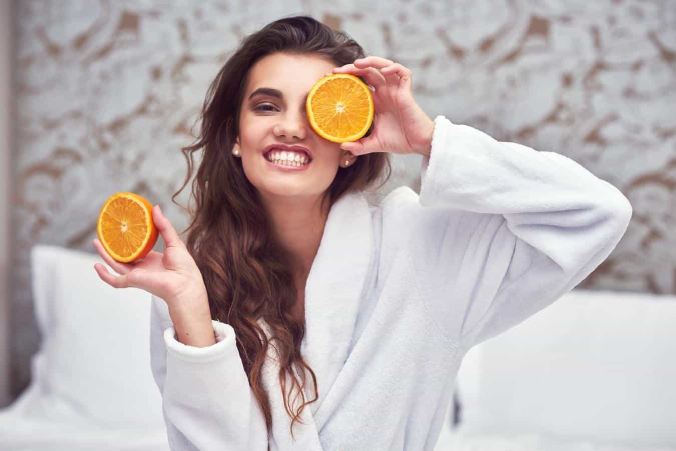woman with long brown hair smiling and holding up two oranges